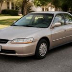 Srebrna Honda Accord zaparkowana przy krawężniku na spokojnej, zielonej ulicy osiedlowej